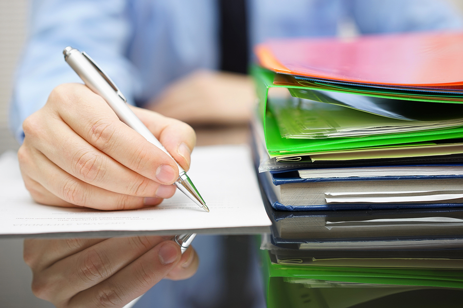 A businessperson takes notes and reviews a stack of documents in a folder.